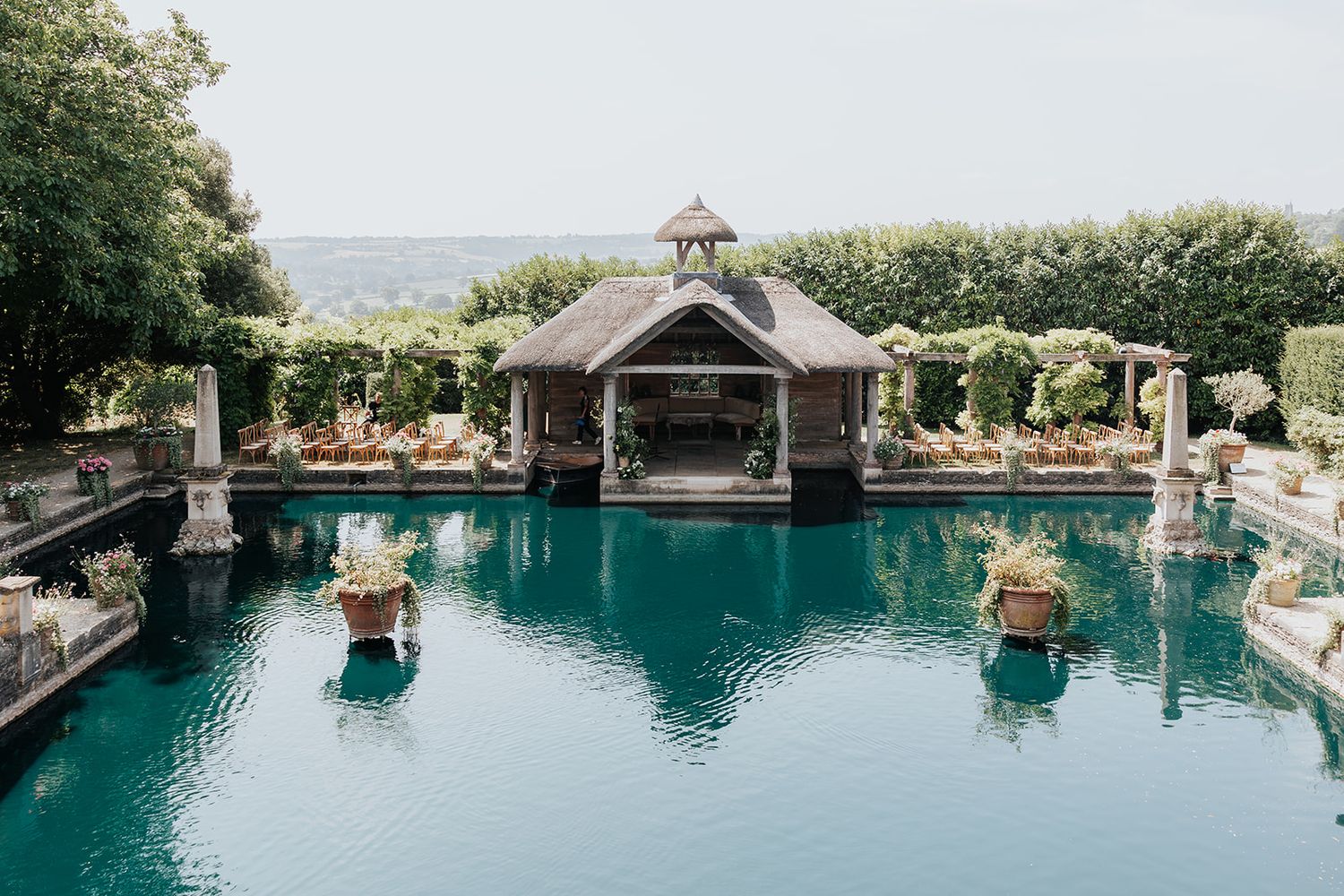 Elegant outdoor pool with teal water, ornate statues, lush greenery, and a charming gazebo overlooking the ocean.