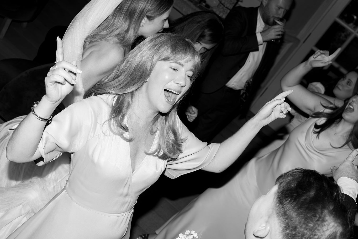 Woman dancing joyfully at a wedding reception with arms raised in black and white photography.