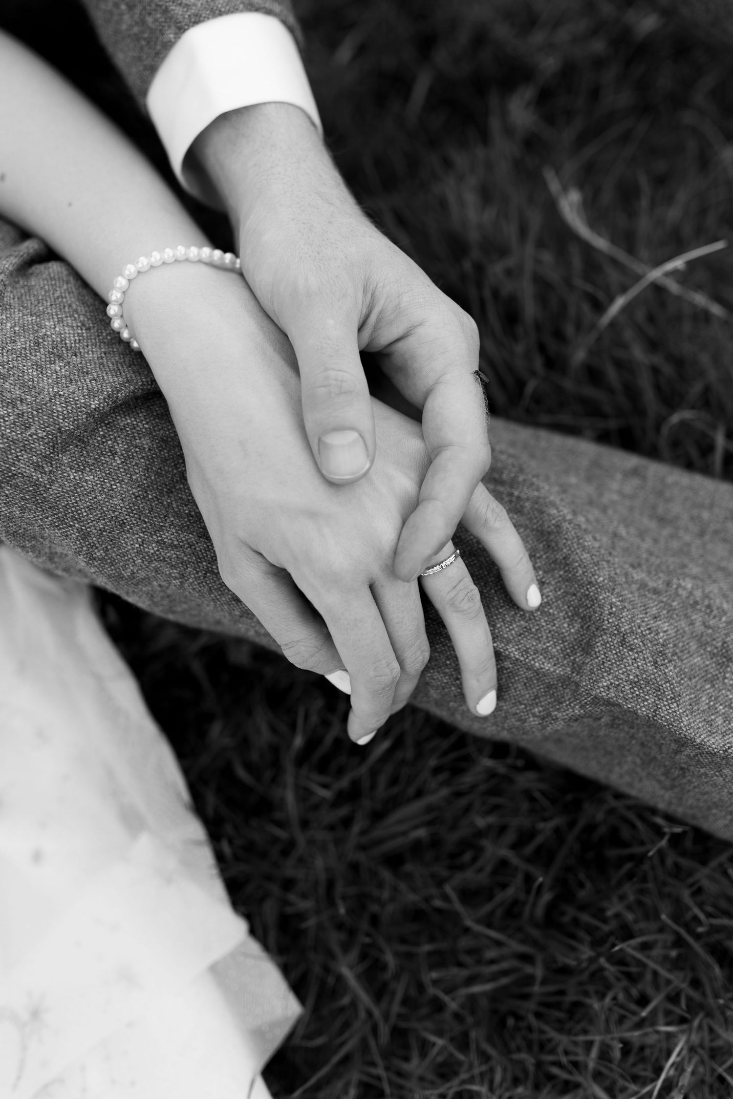 A close-up black and white image of two hands clasped together on a grassy surface.