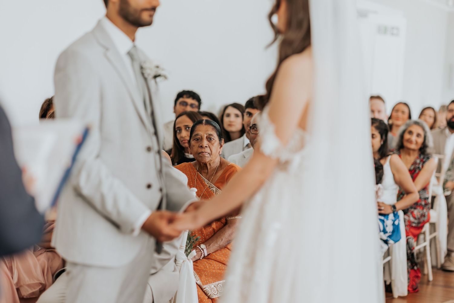 Guests watching emotional wedding ceremony as bride and groom exchange vows in bright white venue.