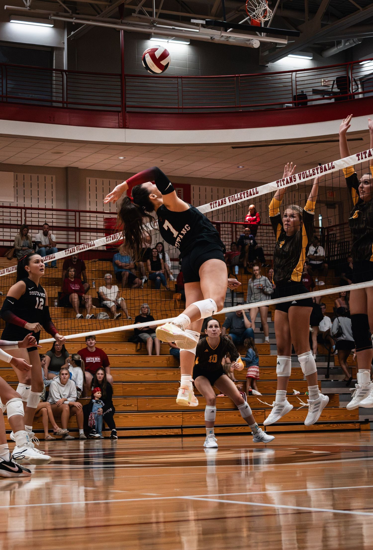 IUSB volleyball players competing at the net during an indoor college volleyball match.
