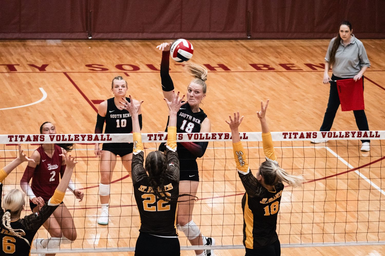 IUSB volleyball players defending at the net as an opposing player attacks the ball during a match.