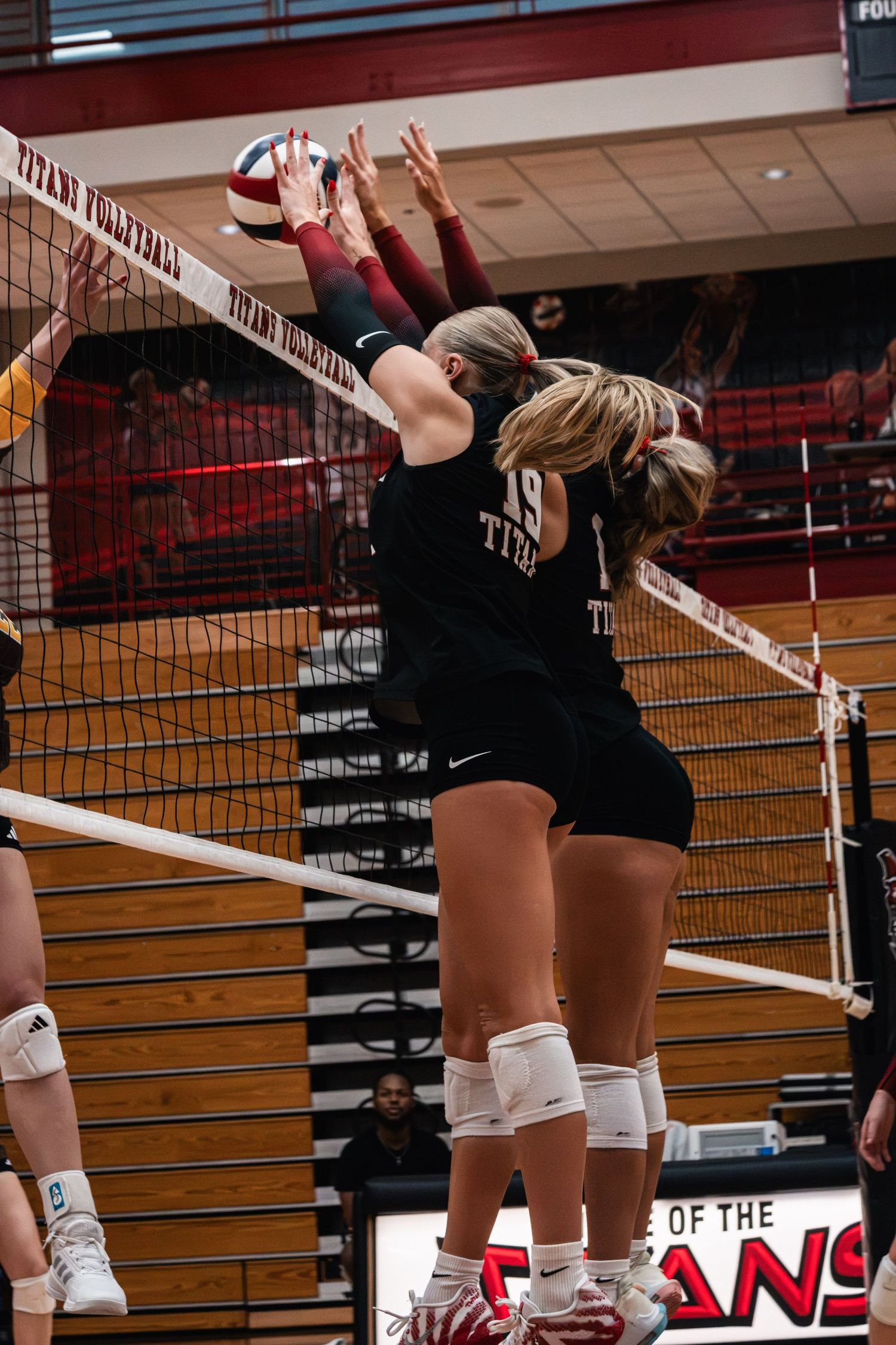 IUSB volleyball player reaching above the net to attack the ball during a college match.