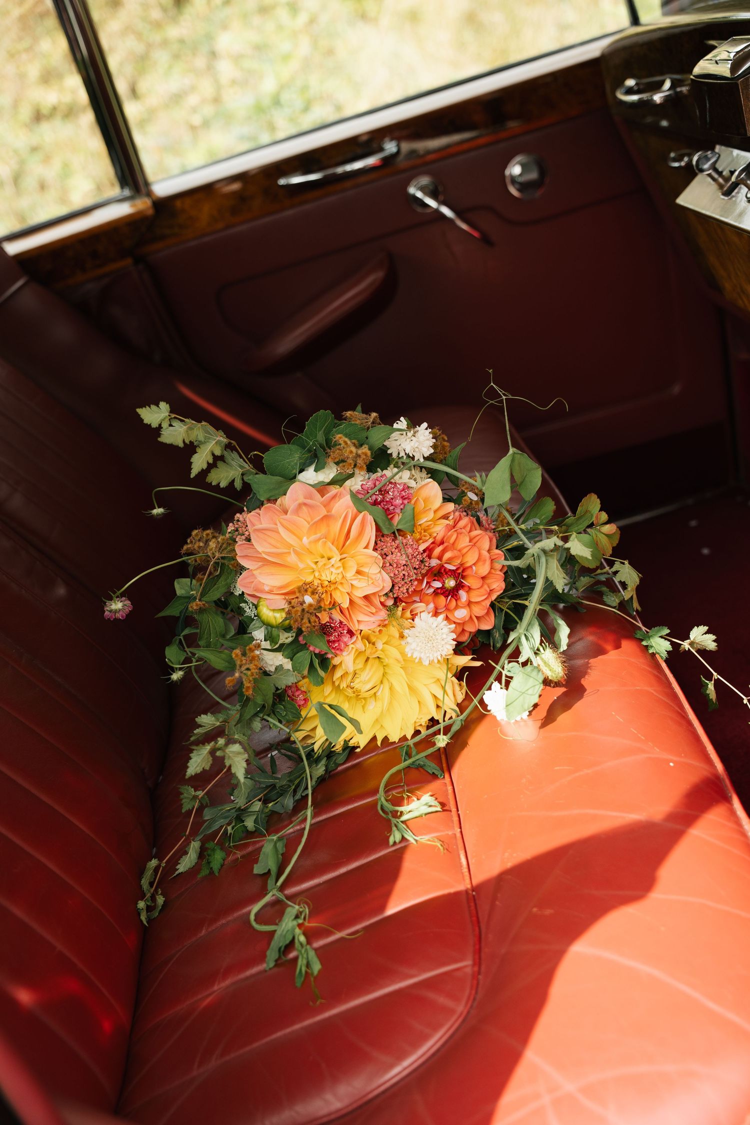 Colorful autumn wedding bouquet with orange dahlias on vintage red leather car seat.