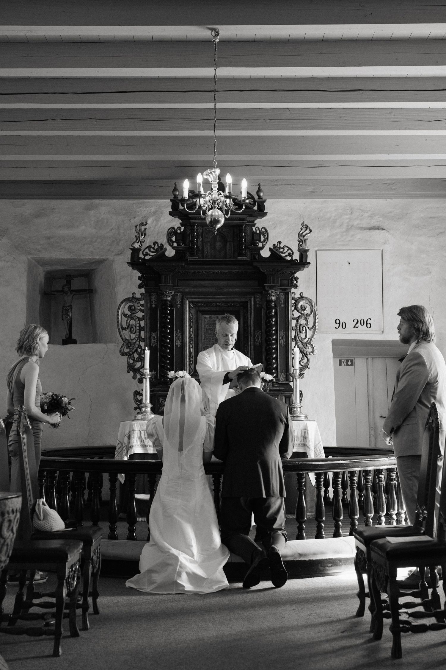 Wedding ceremony inside a historic church with couple kneeling before an ornate altar.