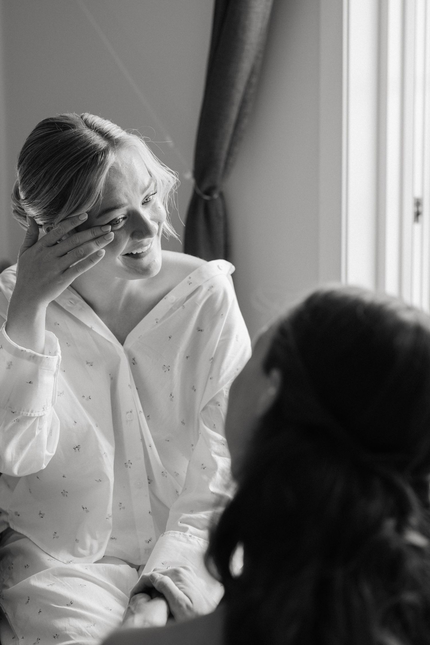 Black and white photo of emotional bride in robe wiping tears during wedding preparations.