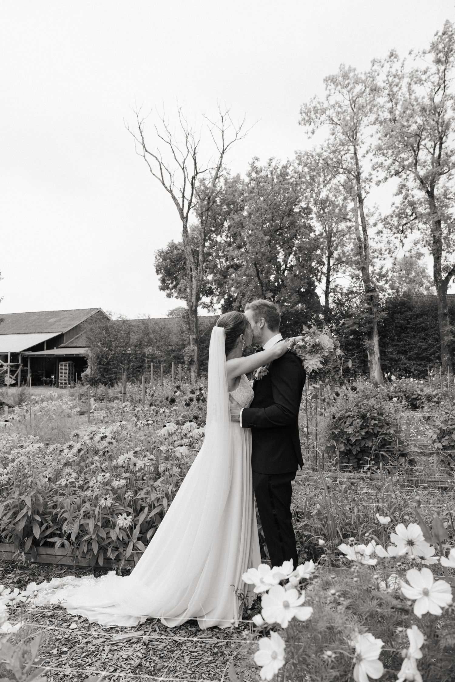 Bride and groom sharing a romantic kiss in a garden setting in a black and white wedding portrait.