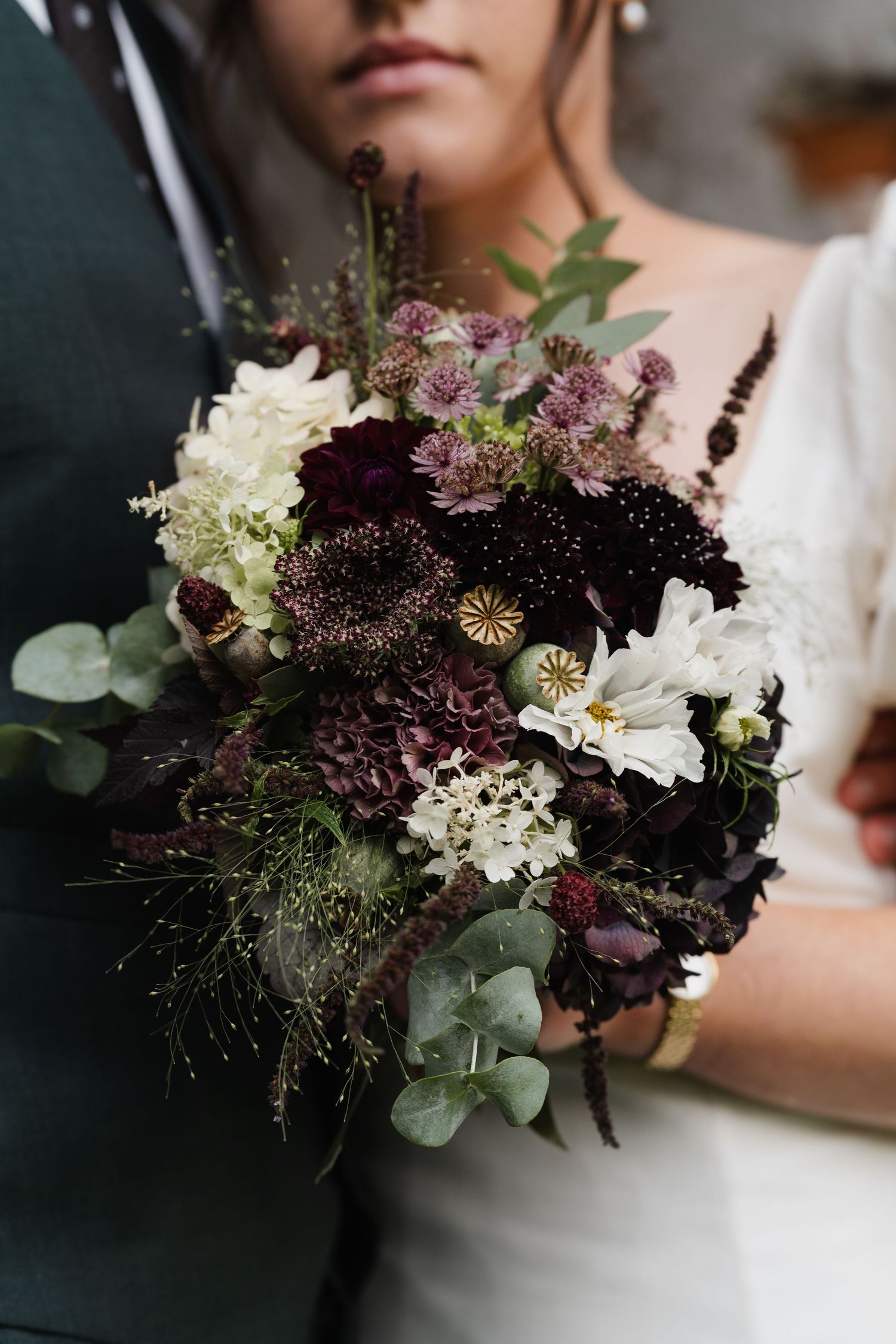 Close-up of a dramatic bridal bouquet featuring deep purple, burgundy, and white flowers with eucalyptus.