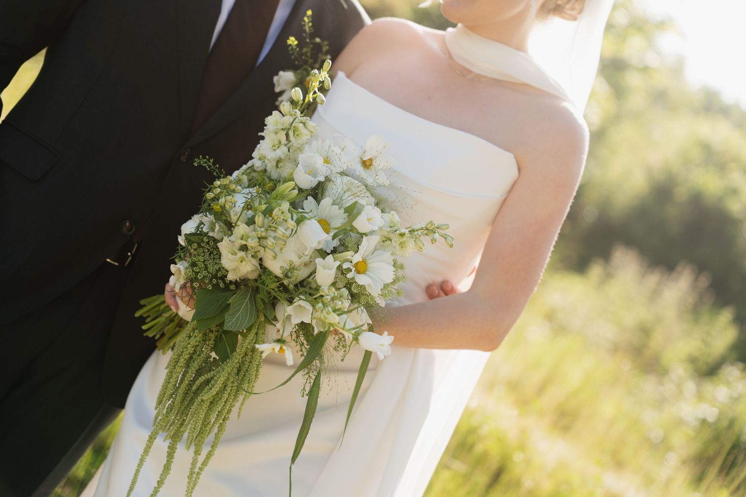 Close-up of bride holding elegant white and green wedding bouquet with cascading greenery.