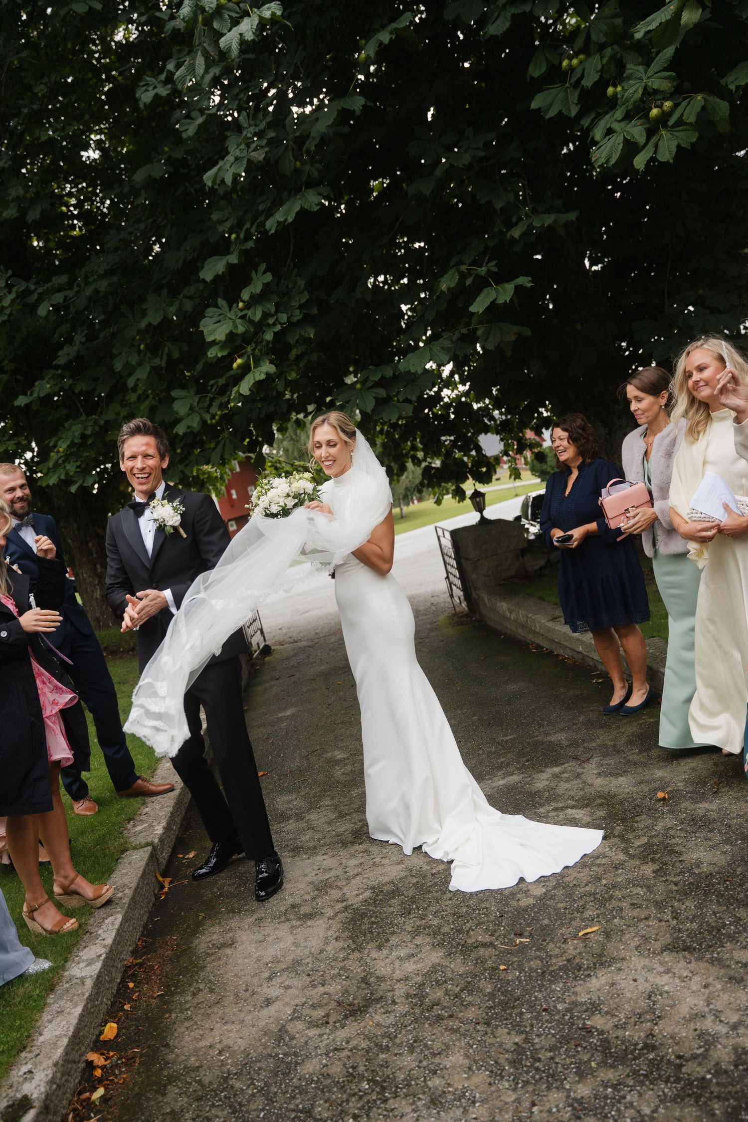 Groom lifts bride in white gown as wedding guests celebrate with confetti outdoors.