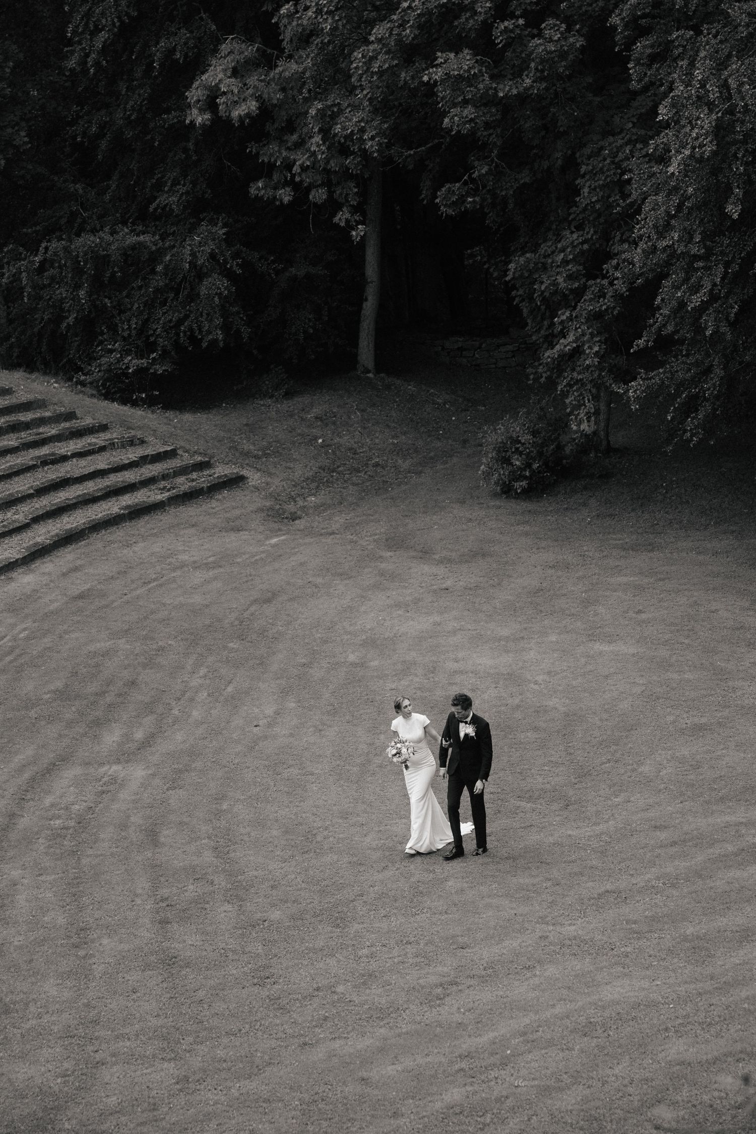 Black and white aerial photo of bride and groom walking on a manicured lawn.