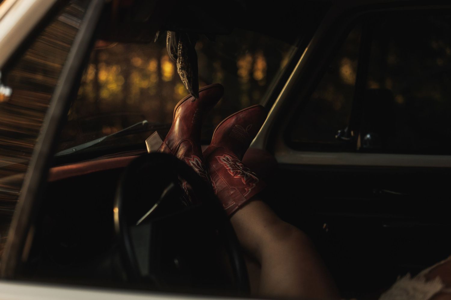 Gloved hand gripping a steering wheel inside a vintage car, with dramatic lighting and forest background.