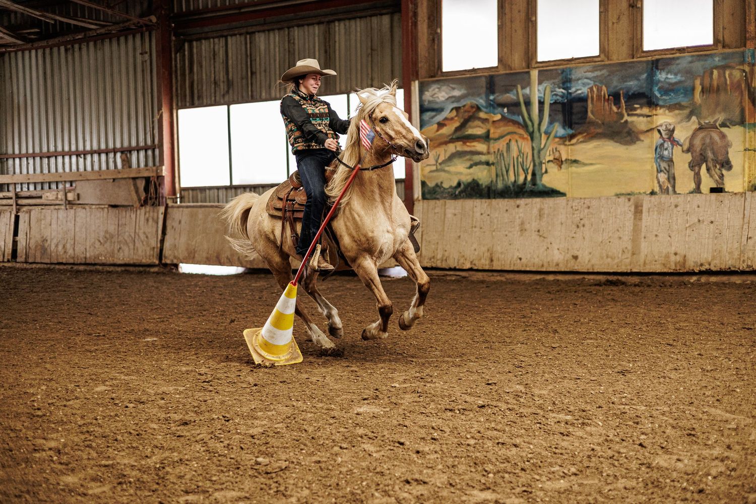 Western rider on a palomino horse navigating orange cones in an indoor arena. Pole Bending.