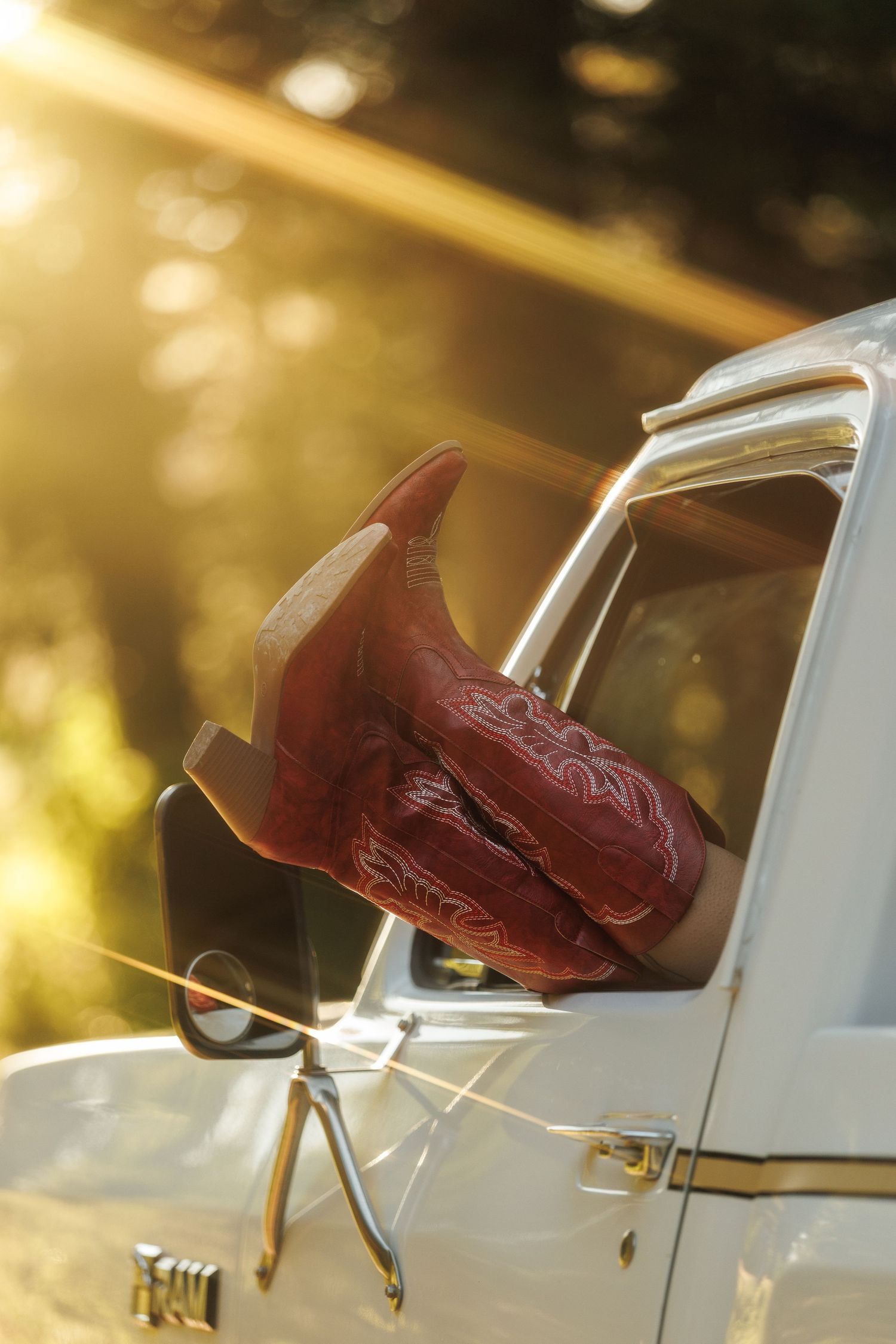Red cowboy boots resting on a white truck window in golden sunset light with bokeh background.