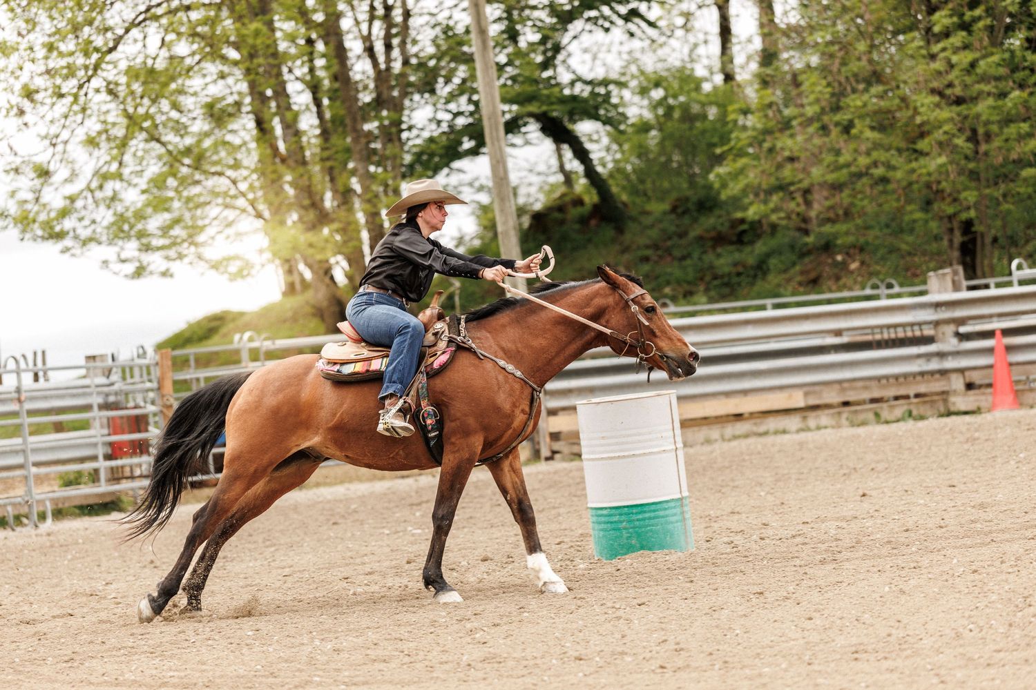 Cowgirl riding a brown horse around a barrel in a sandy rodeo arena during a barrel racing competition.