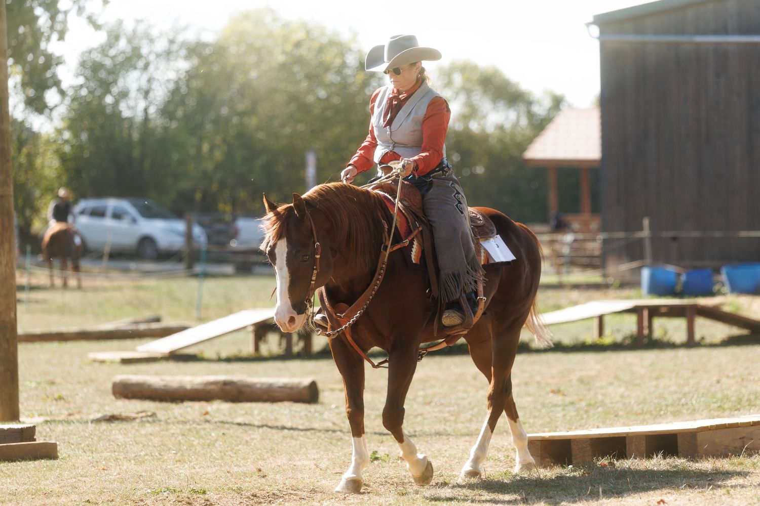 A rider in western attire on a chestnut horse in an outdoor arena during a sunny equestrian event.