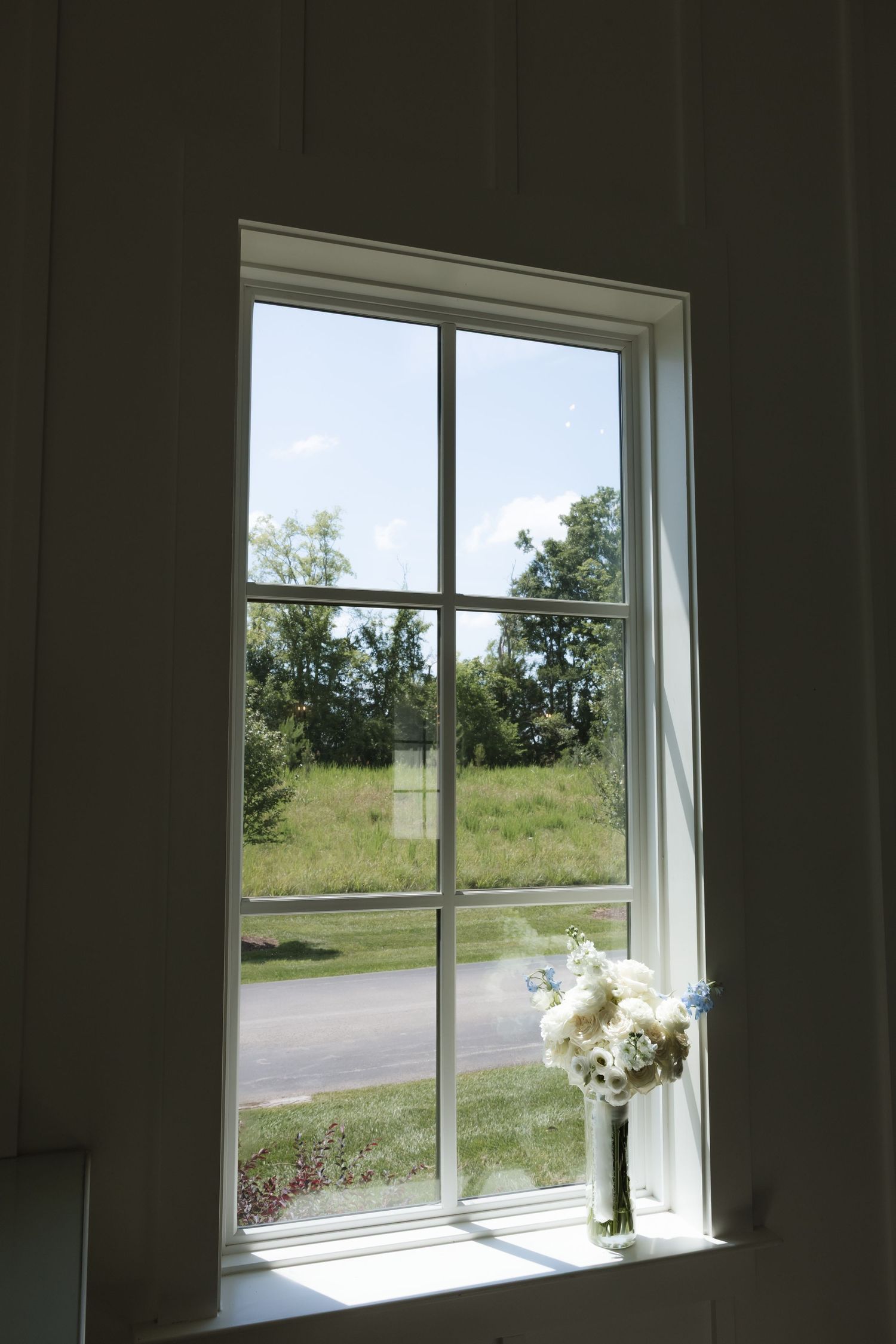 White wedding bouquet on windowsill overlooking green landscape on sunny day.