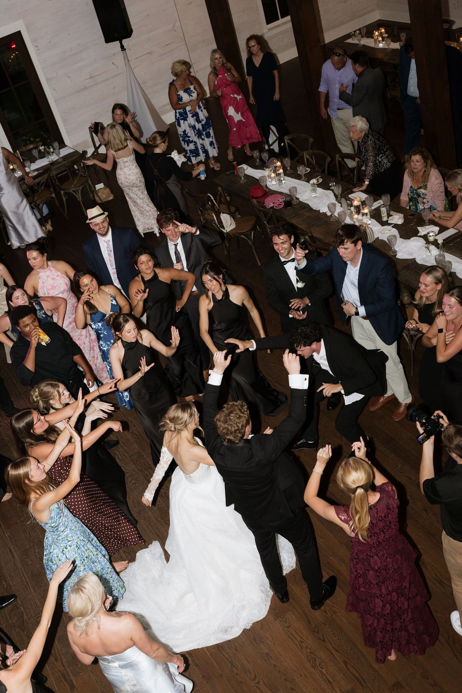 Bride and groom dancing with wedding guests on crowded reception dance floor celebration.