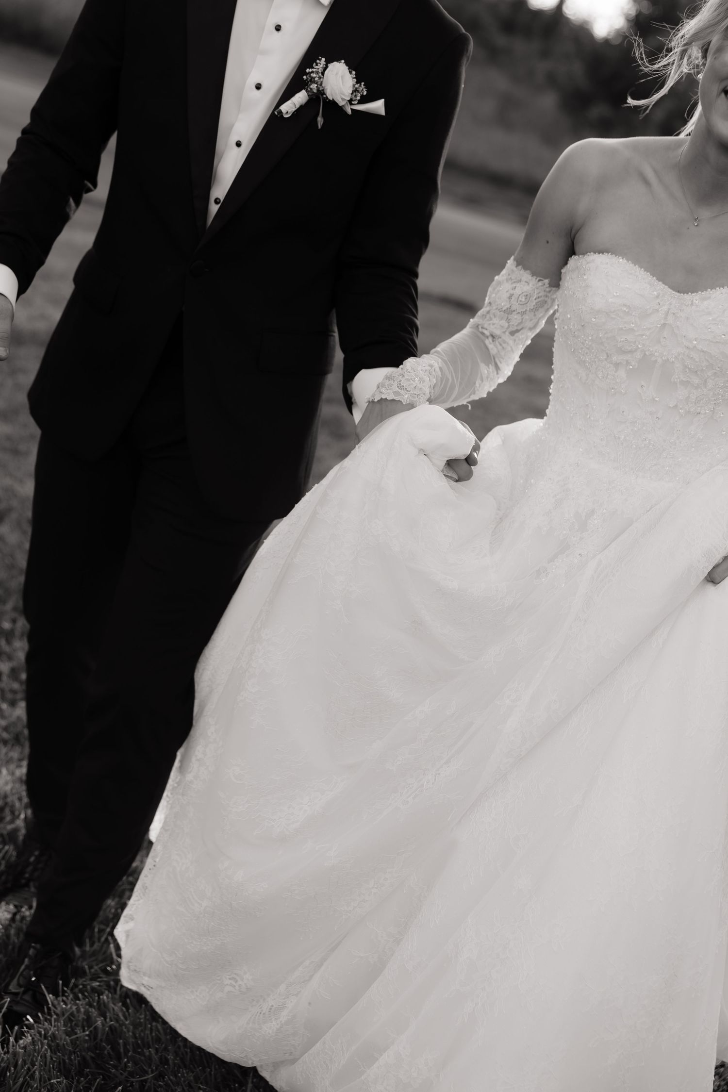 Black and white photo of bride in ballgown and groom in tuxedo holding hands at wedding ceremony.