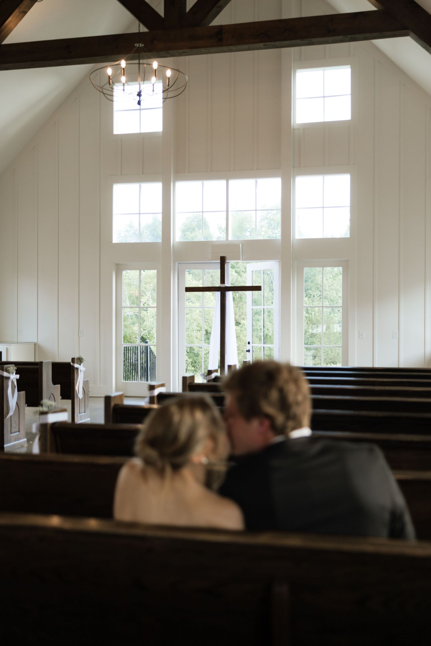 Bride and groom sit together in church pews facing a wooden cross during wedding ceremony.