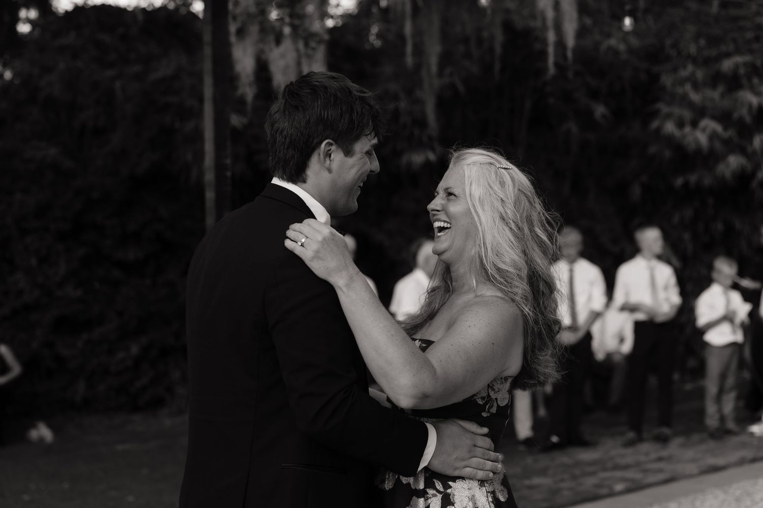 Black and white photo of a couple sharing a joyful first dance at an outdoor wedding reception.