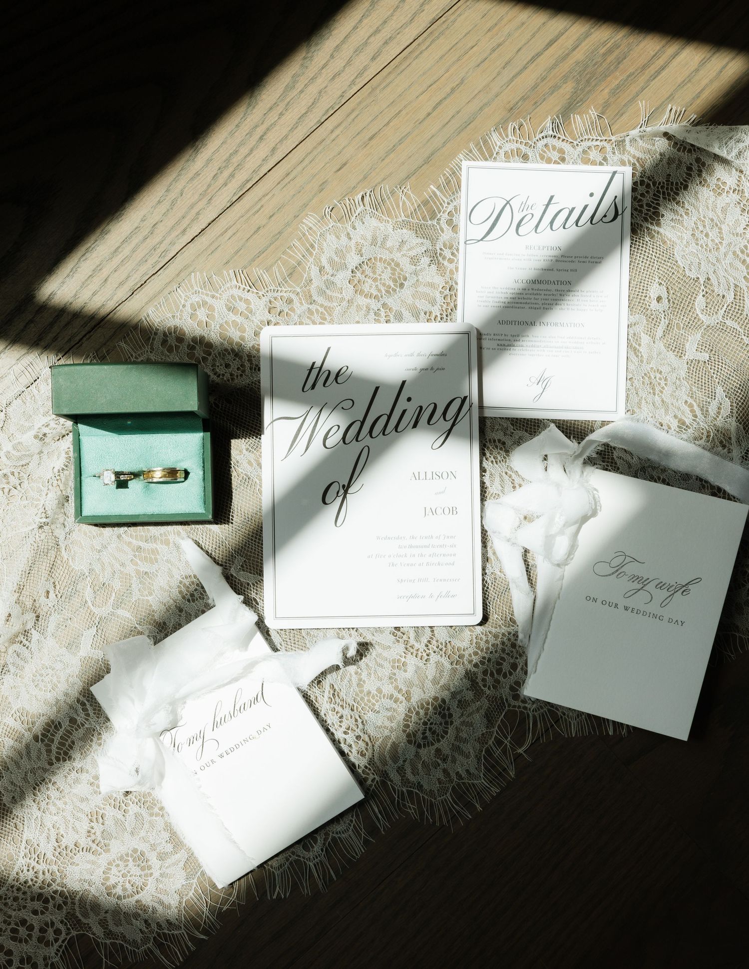 Wedding stationery flat lay featuring invitation suite, details card, ring box, and lace accents in natural light.