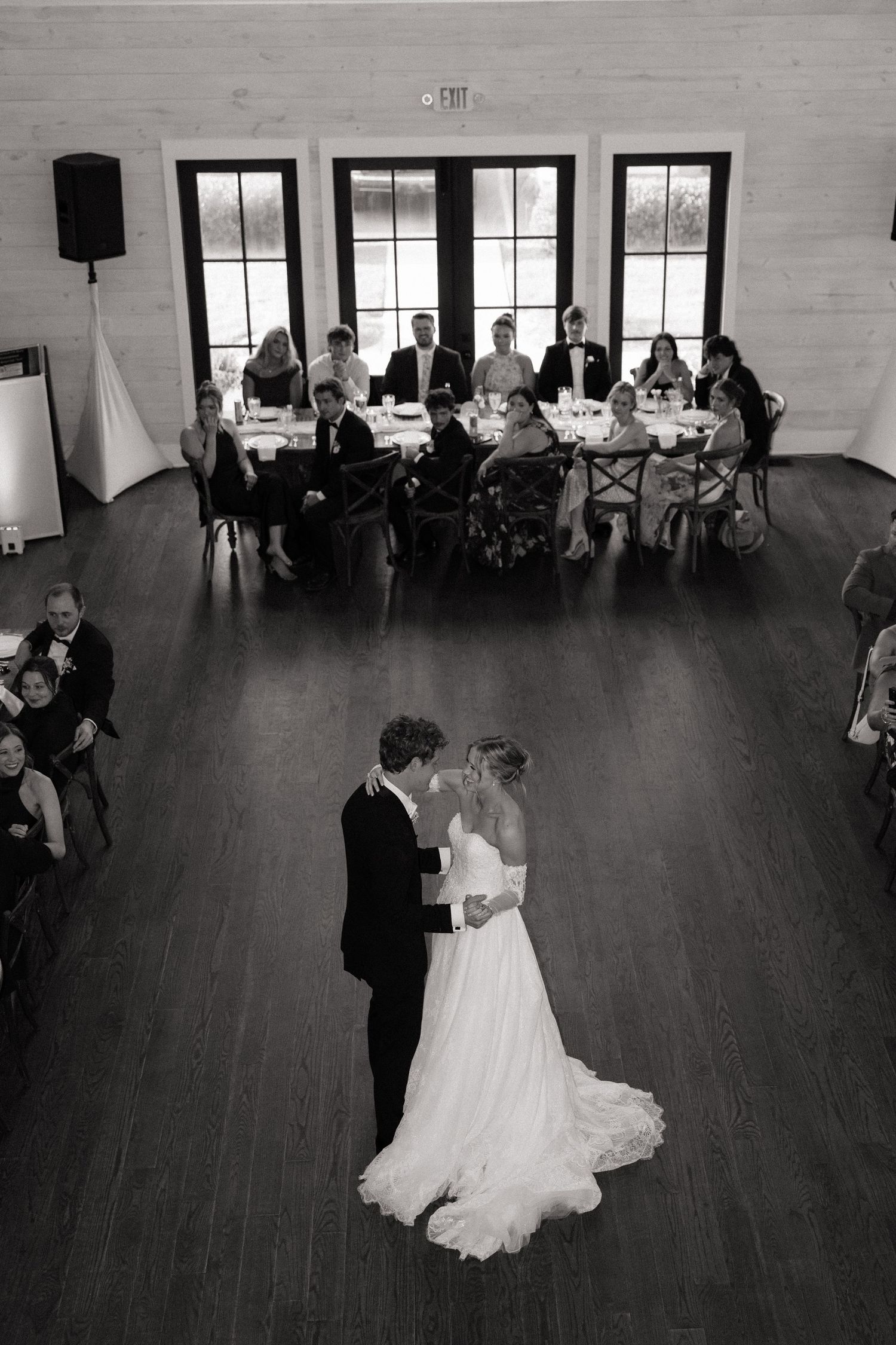Bride and groom share their first dance as wedding guests watch in a black and white reception photo.