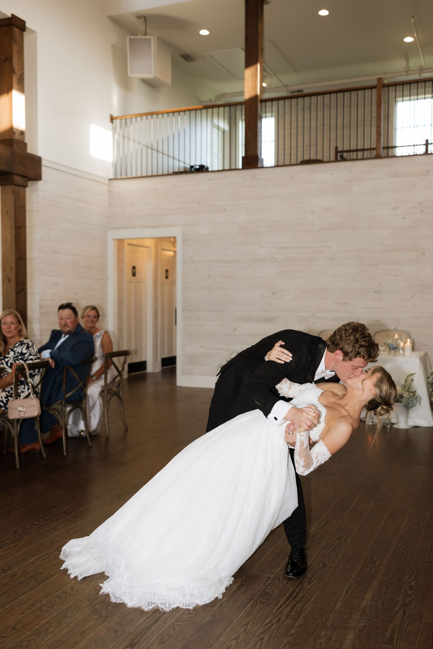 Groom dips bride for a romantic kiss during their first dance at a modern wedding reception venue.