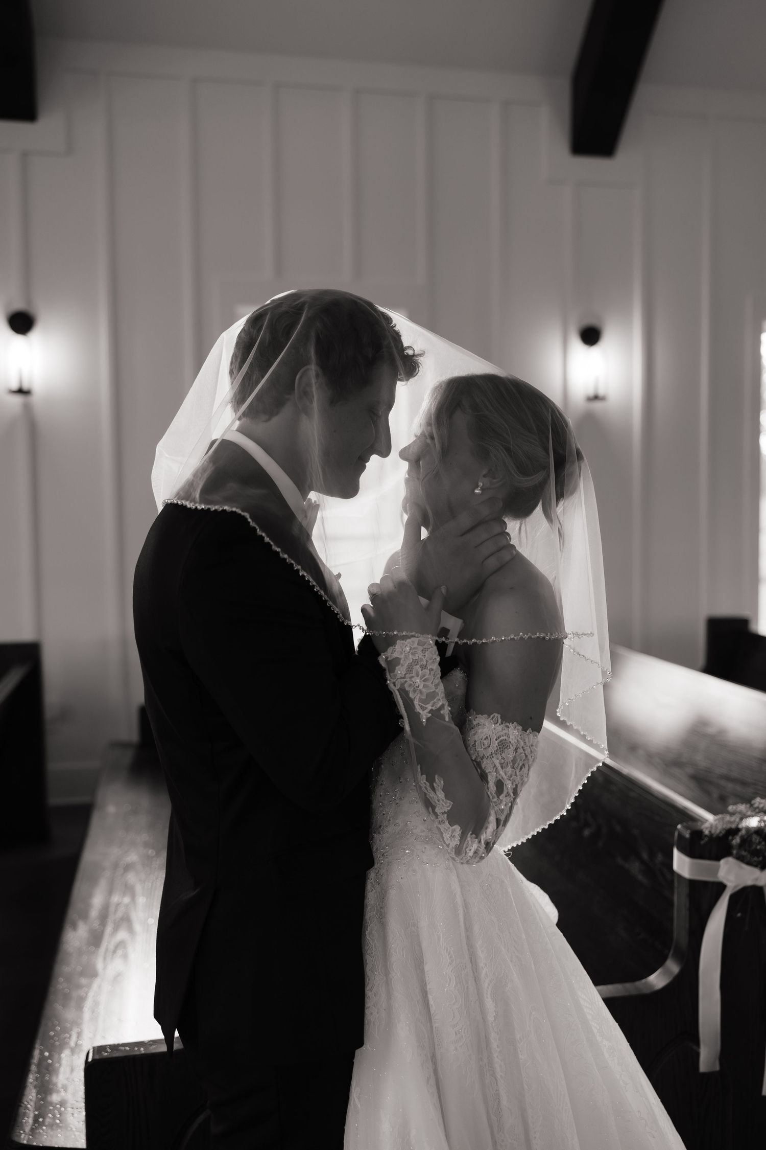 Black and white photo of bride and groom sharing intimate moment under veil in chapel.