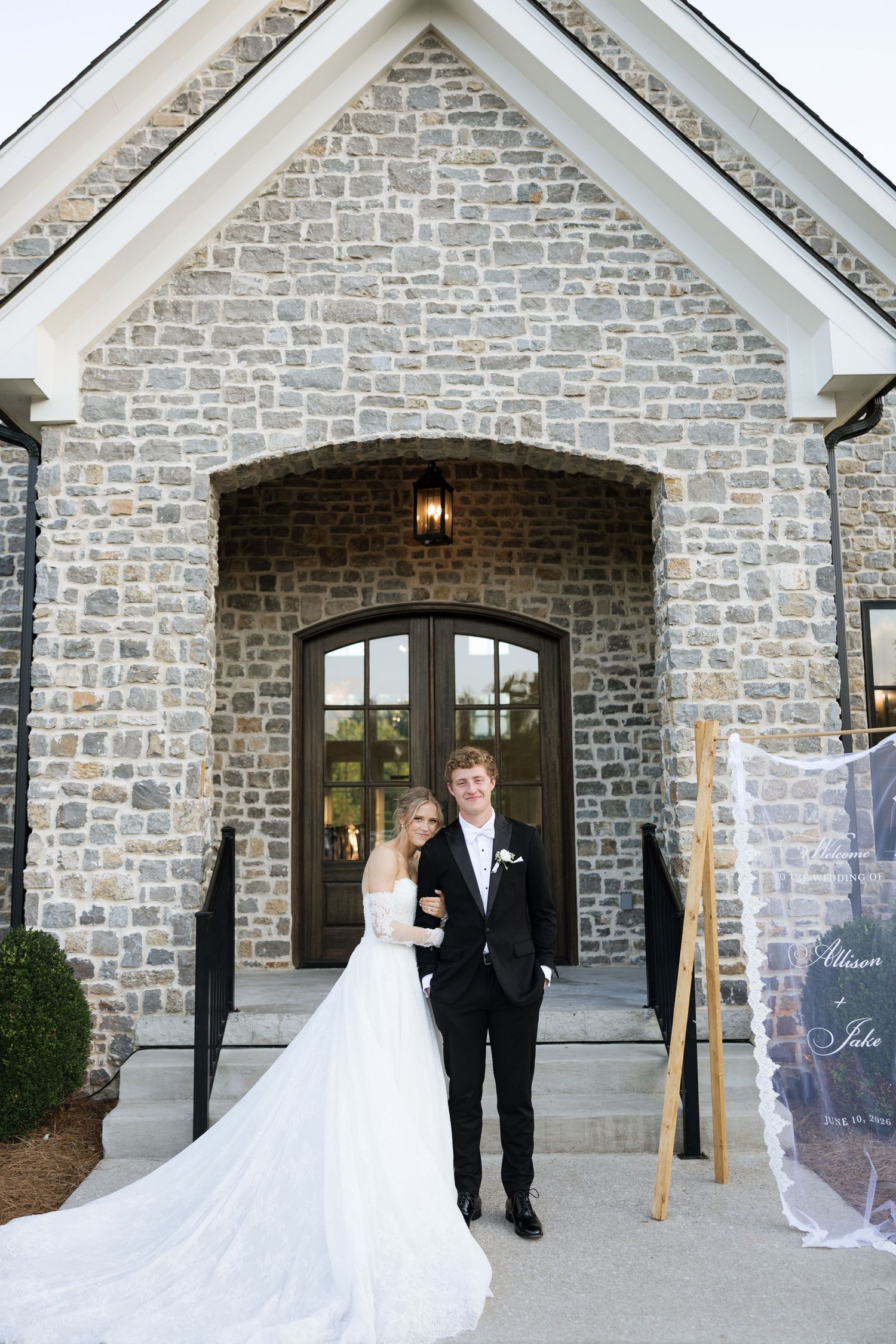 Bride and groom pose together outside a stone chapel wedding venue with elegant double doors.