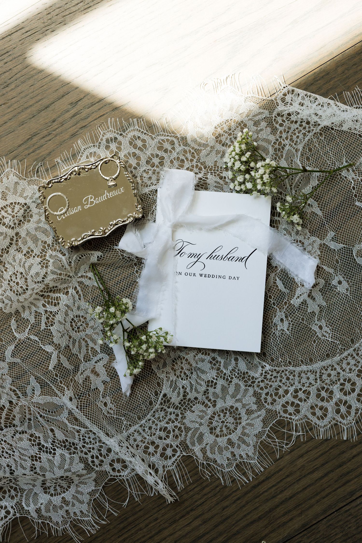 Elegant wedding flat lay with lace veil, gold rings, baby's breath, and a heartfelt card reading To My Husband on our wedding day.