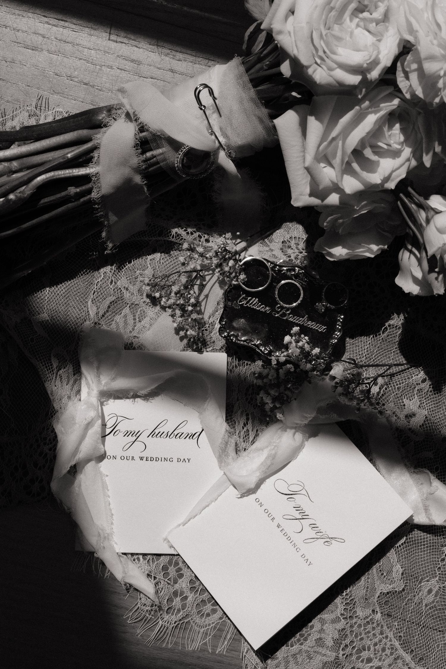 Black and white flat lay of wedding rings, vows cards, and floral bouquet.