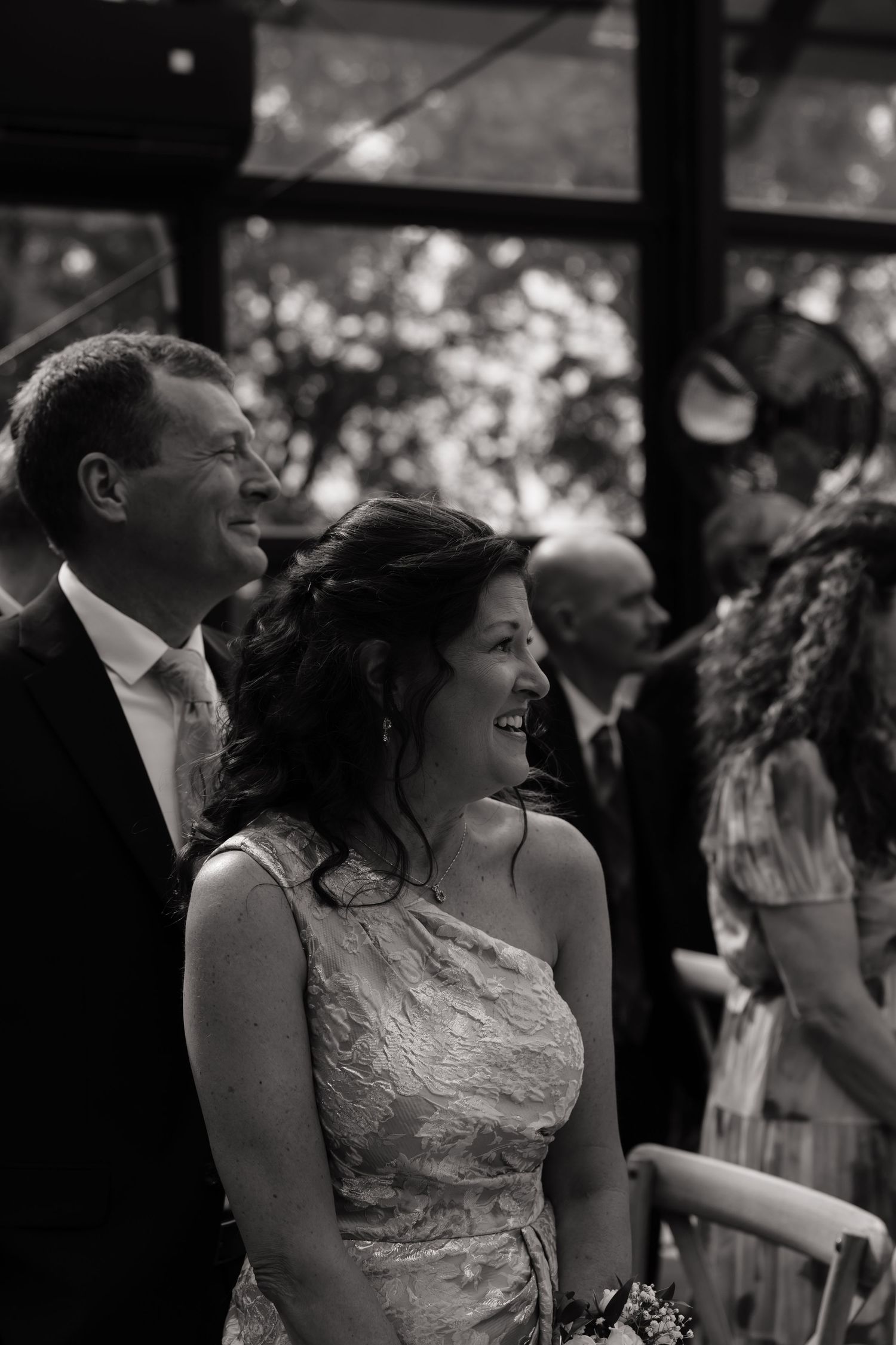Black and white photo of a smiling couple at a wedding ceremony, woman in elegant dress, man in suit with tie.