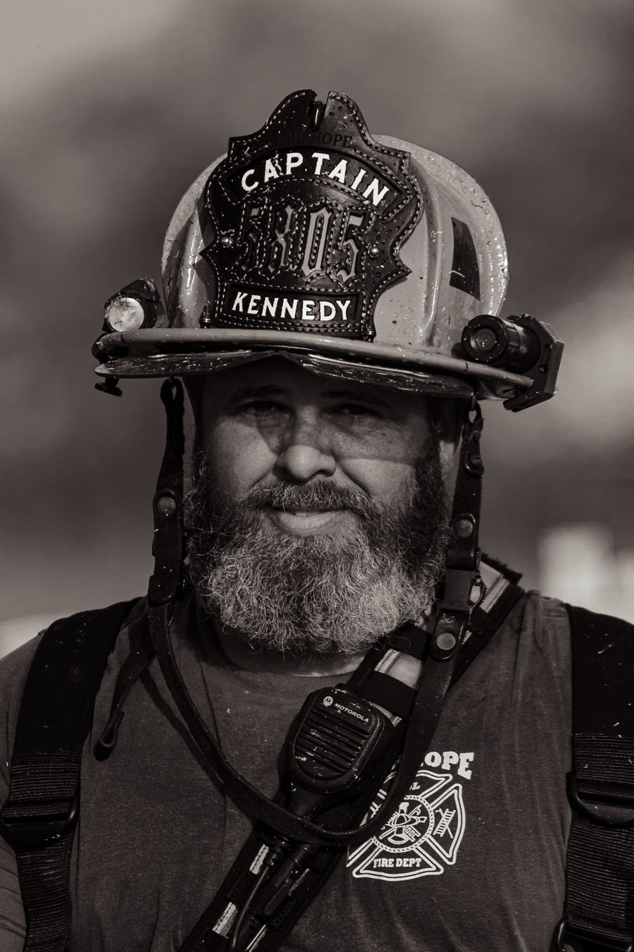 Black and white portrait of bearded fire captain Kennedy in full firefighting gear.