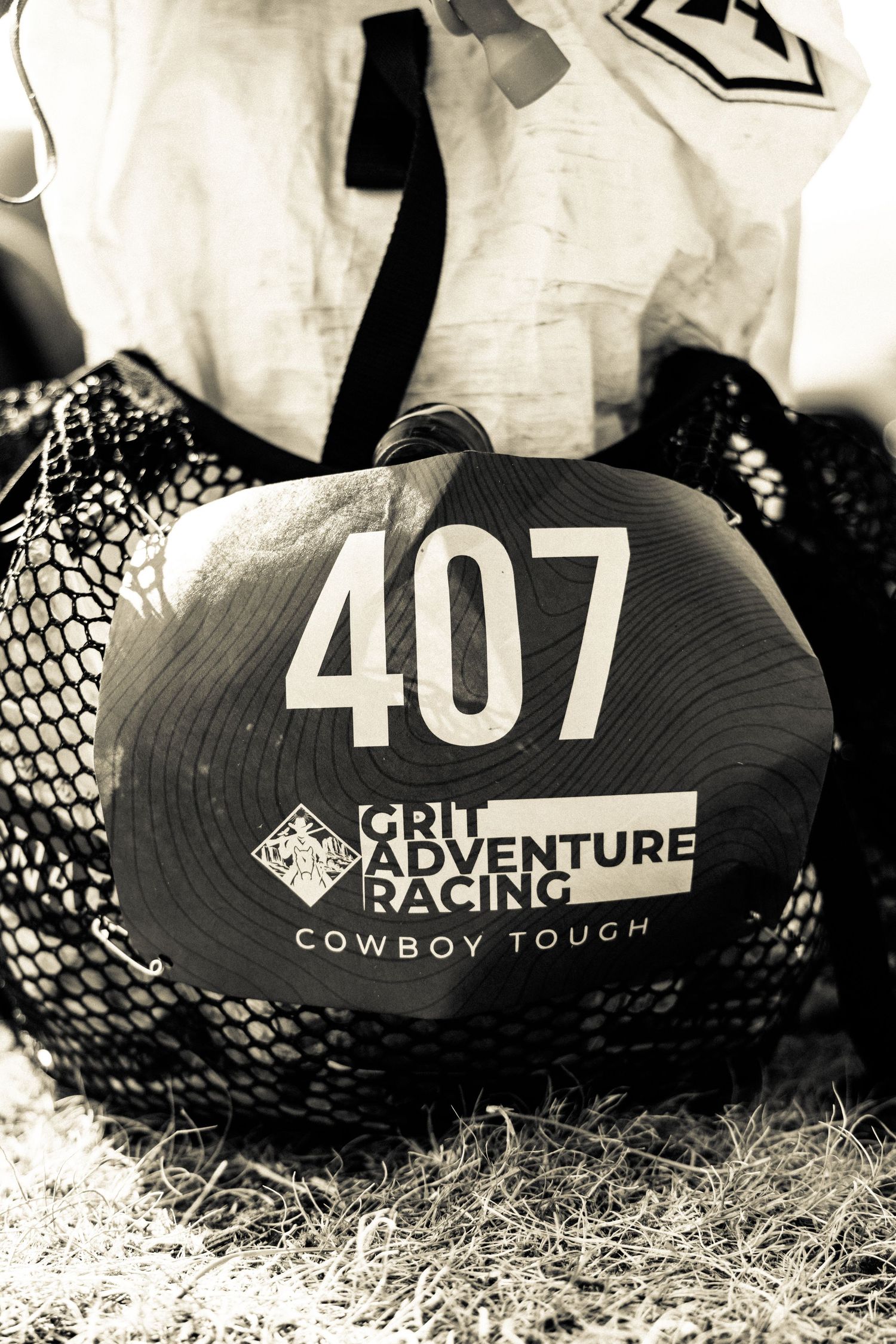 Black and white photo of Grit Adventure Racing Cowboy Tough race number 407 on a hat in mesh bag.