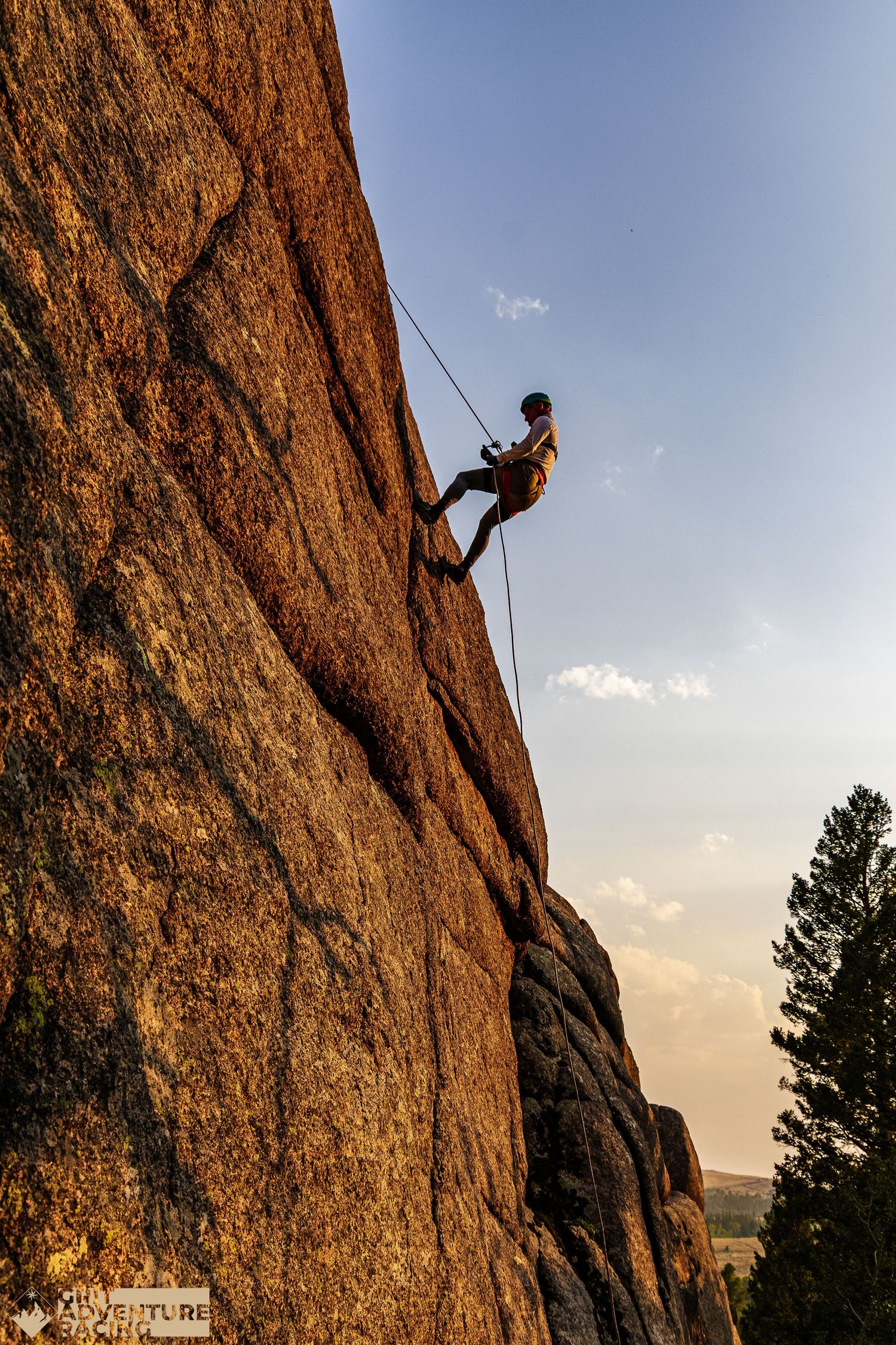 Rock climber rappelling down a steep granite cliff face at golden hour with blue sky background.