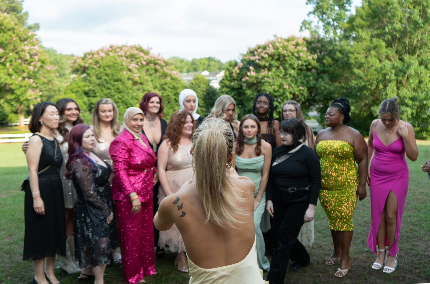 A diverse group of women in formal gowns pose for a group photo outdoors.