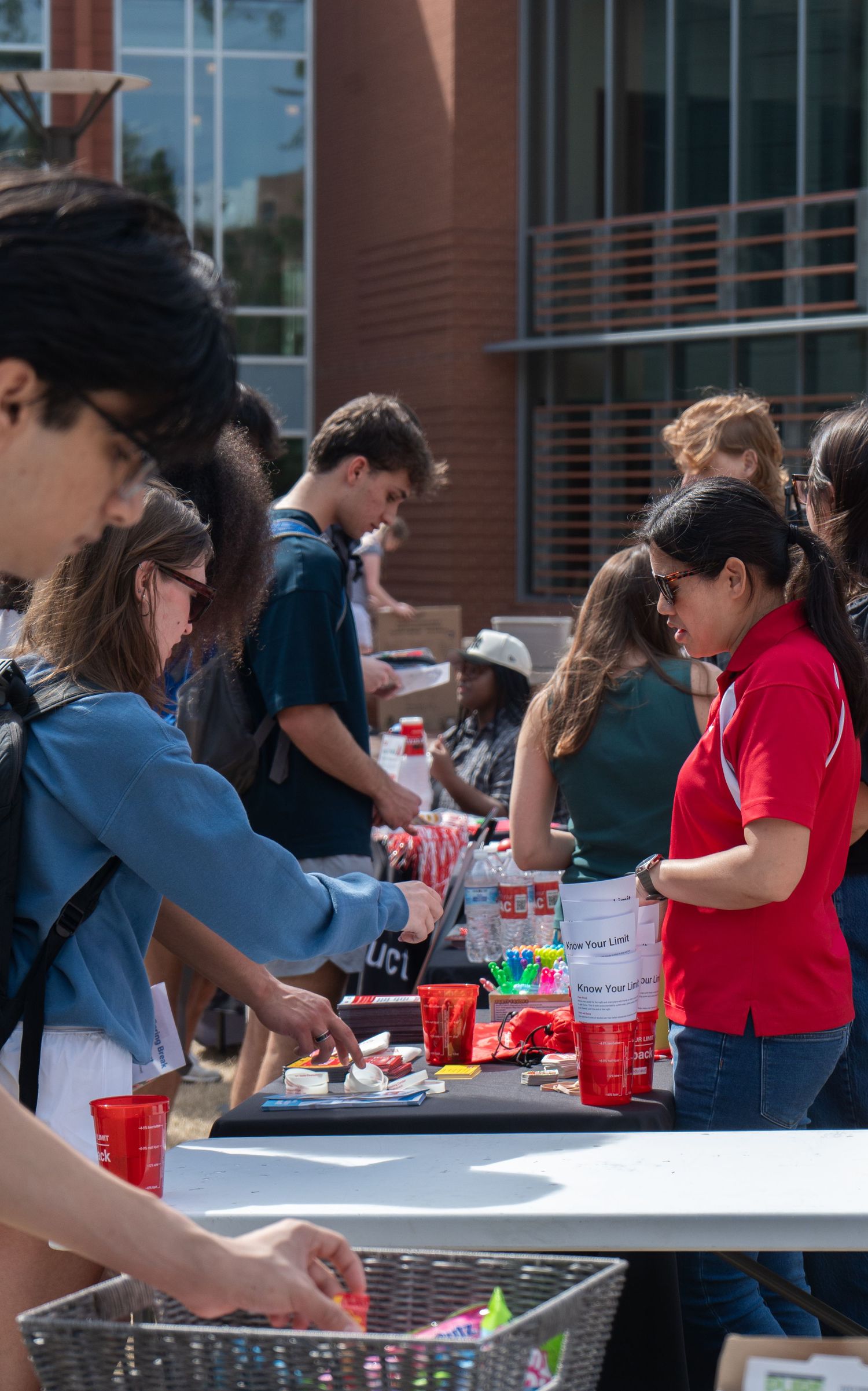 Students browse and pick up items at a table during an outdoor college campus fair event.