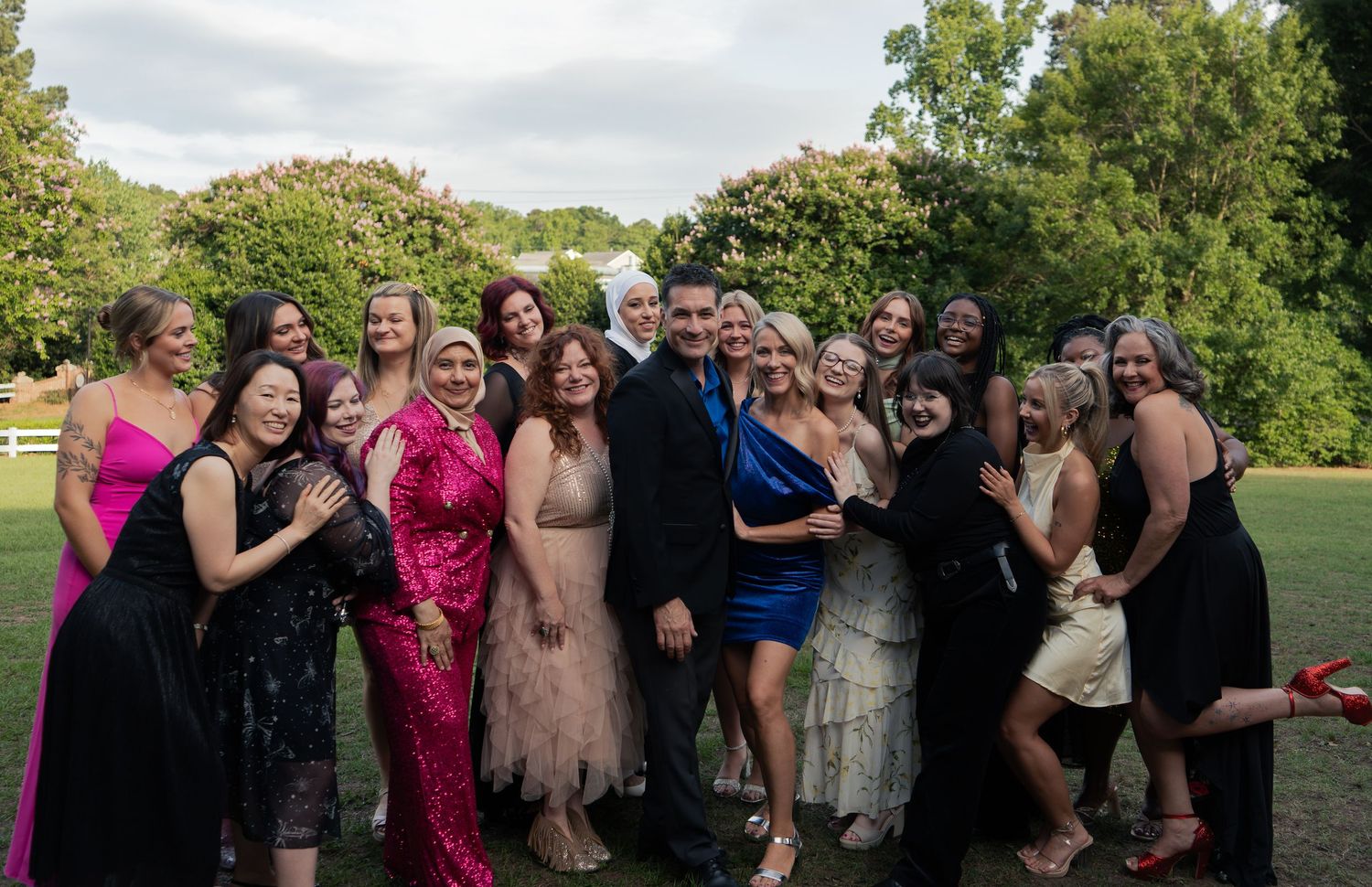 A diverse group of people in formal attire smile together outdoors.