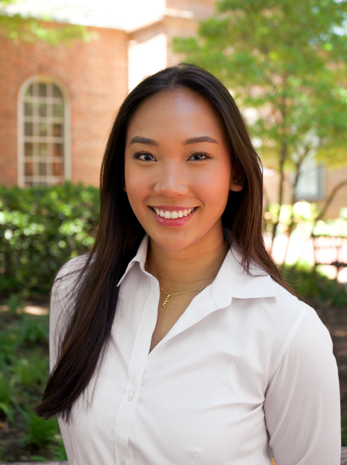 Smiling young woman in white blouse poses for a professional headshot in front of a brick building.