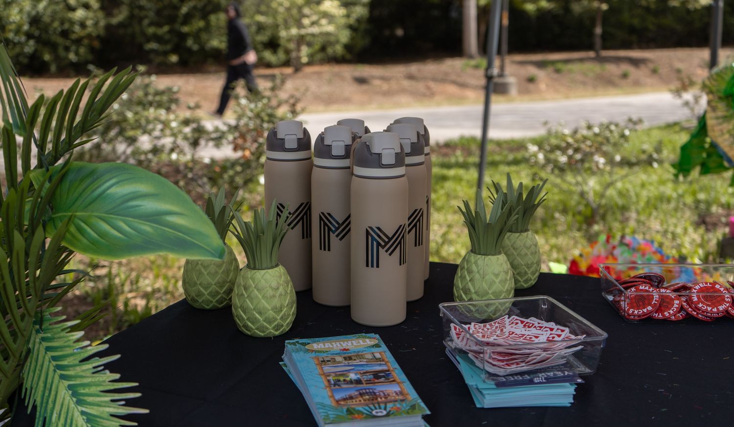 Branded water bottles and pineapple decorations displayed on table at outdoor event booth.