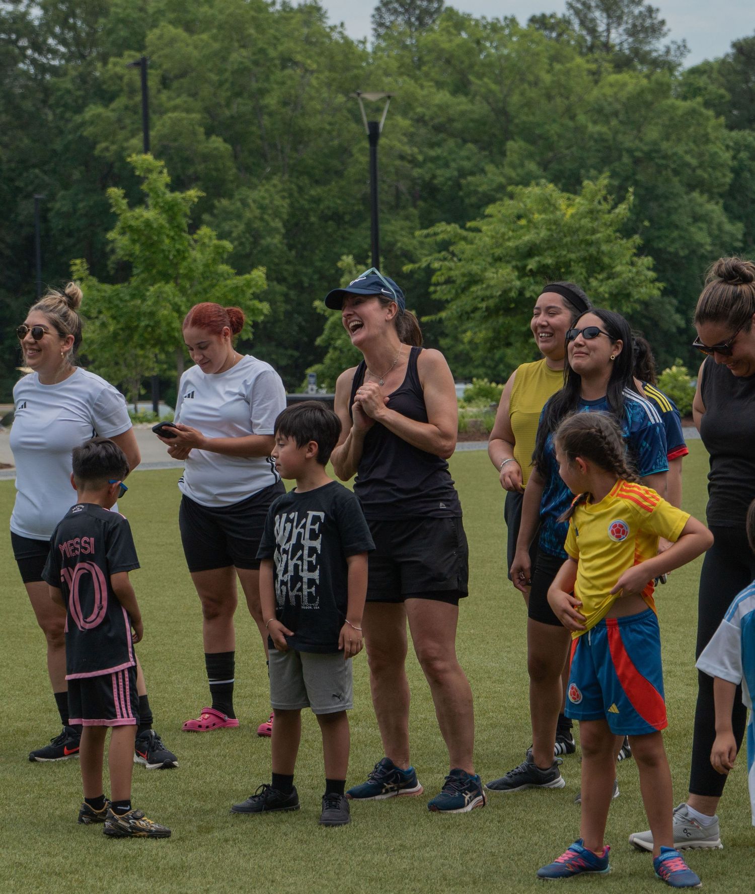 Group of women and children laugh and cheer together on a green sports field outdoors.