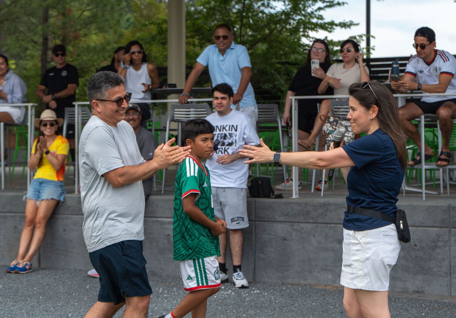 Man and woman reach toward a young boy in a soccer jersey at an outdoor sports event.