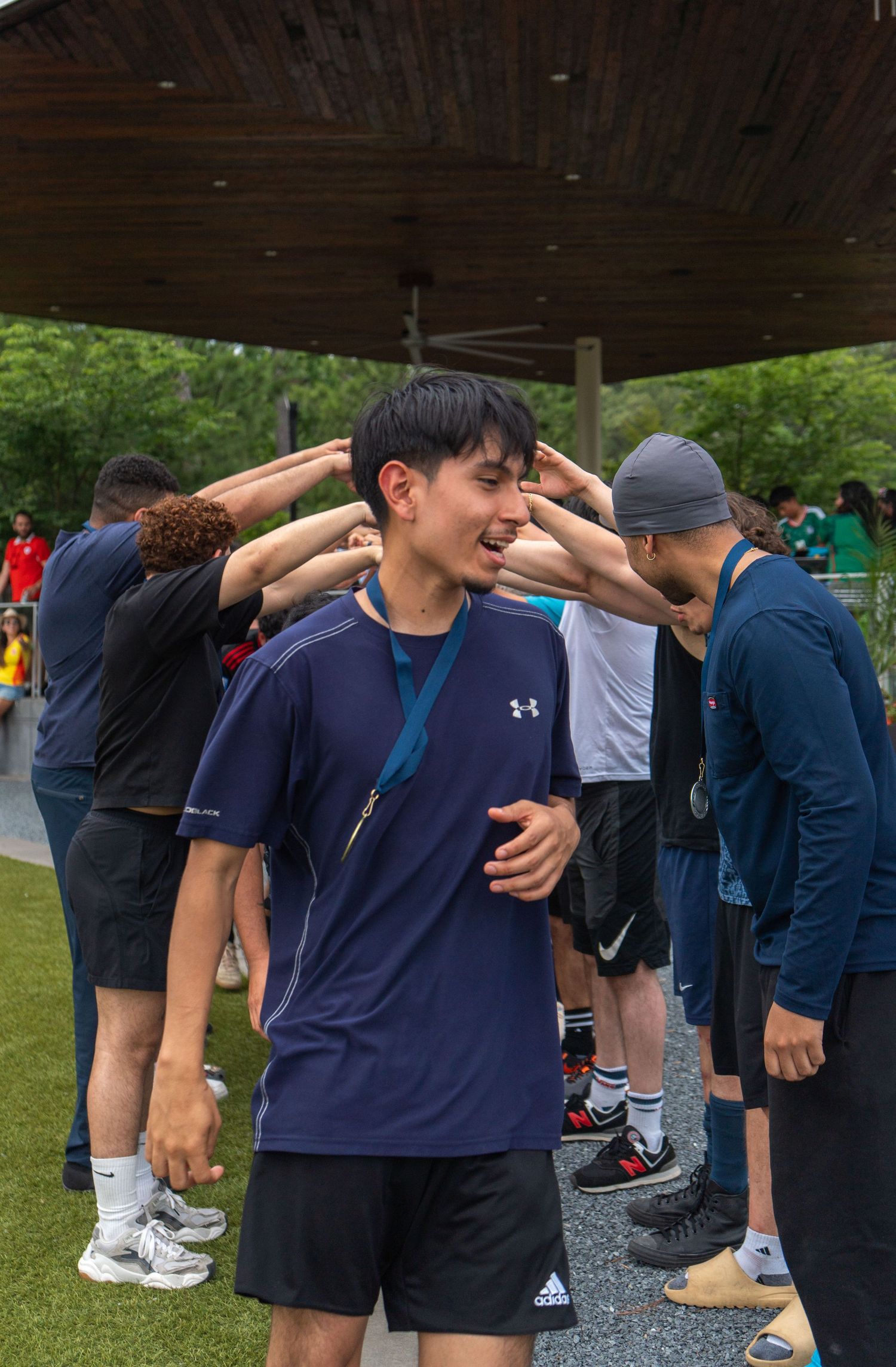 Young man wearing a medal and navy blue shirt smiling at an outdoor sports event.