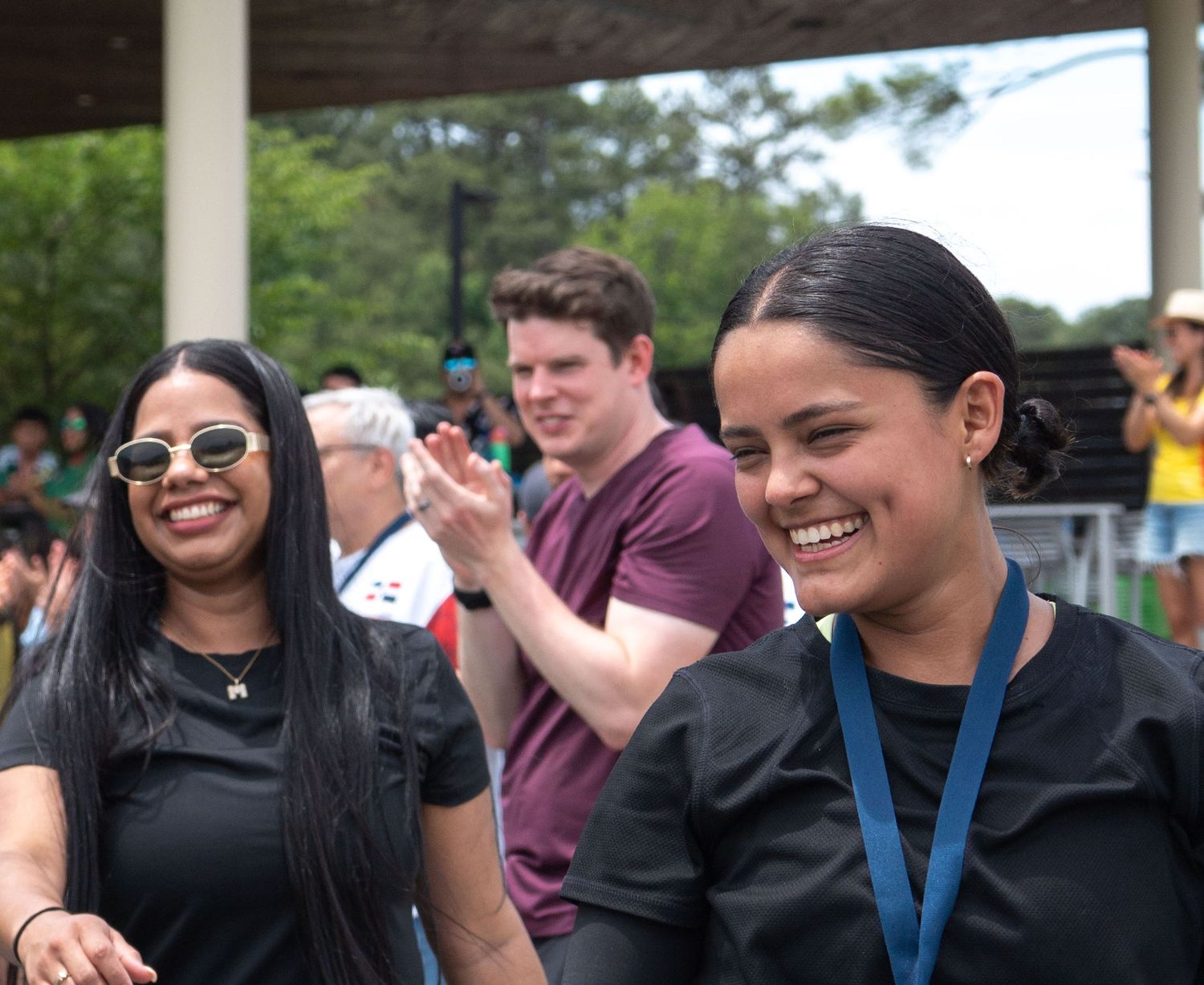 Two smiling women in black athletic wear celebrate at an outdoor community sports event.