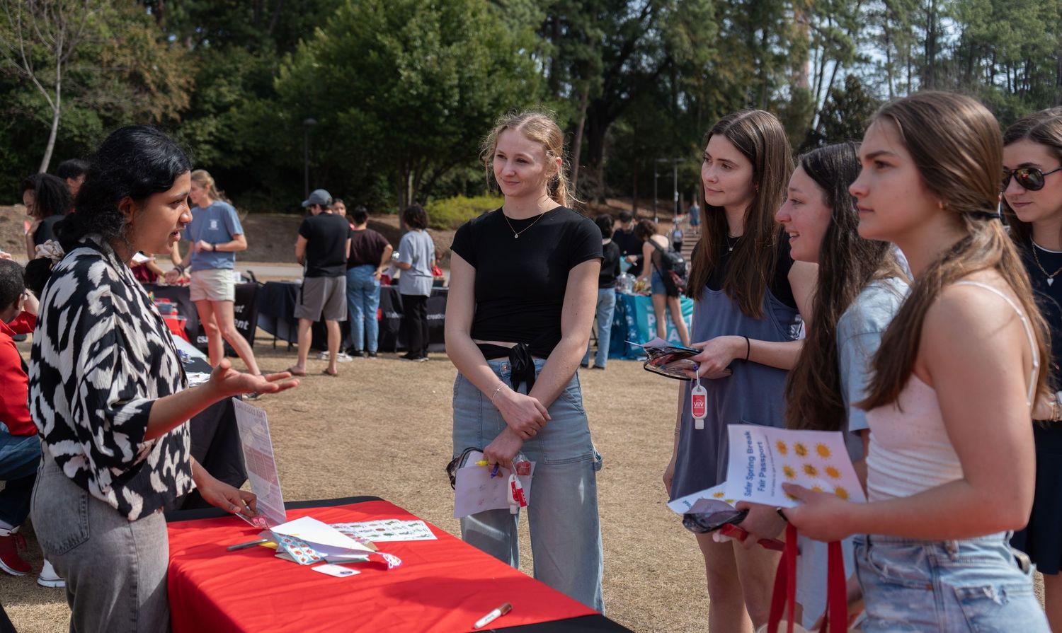 Staff member speaks with group of female students at a red NC State information table outdoors.