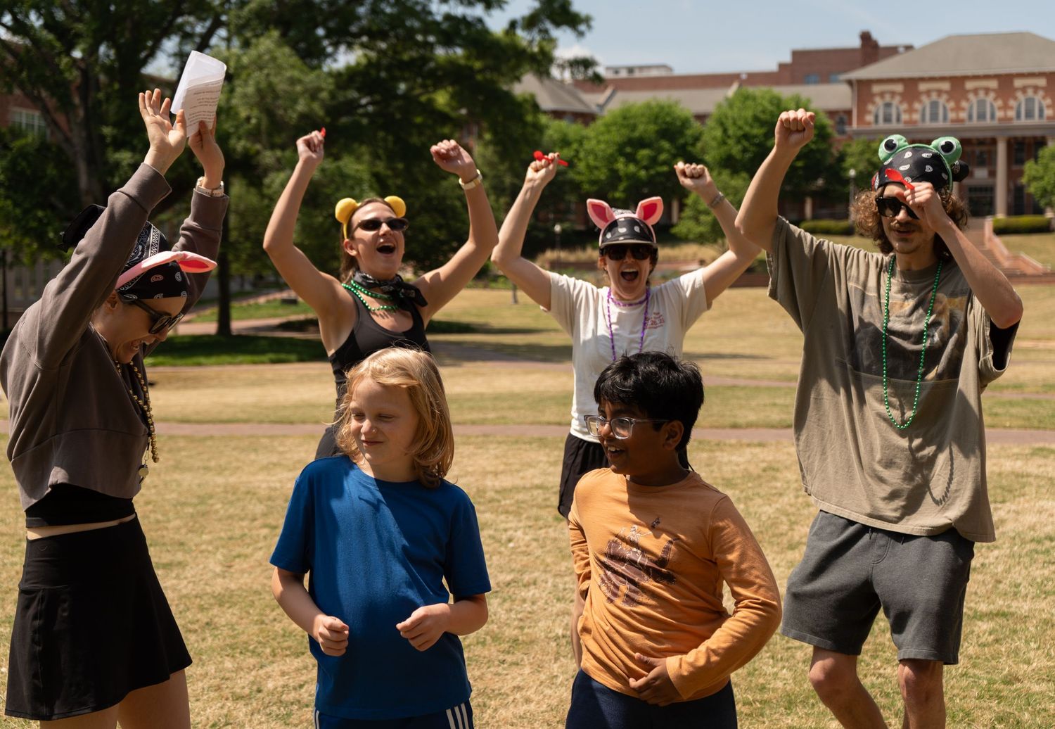 Group of cheerful students celebrating outdoors on NC State campus green lawn.