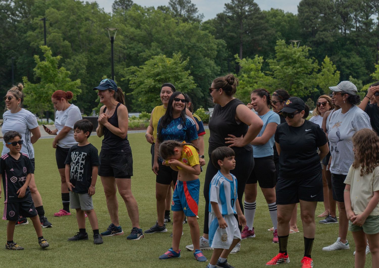 Diverse group of adults and children standing together on a sports field during an outdoor event.