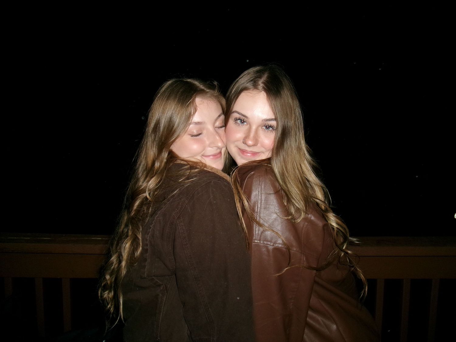 Two young girls with long hair hugging and smiling together at night outdoors.