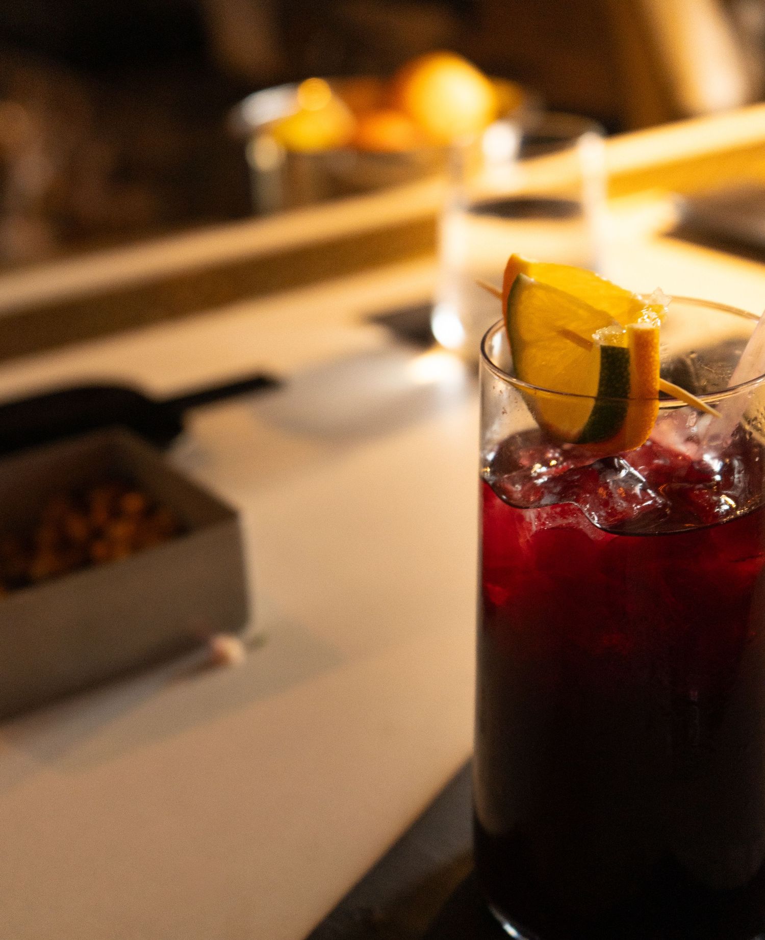Dark red cocktail garnished with a lemon slice and ice in a glass on a bar counter.